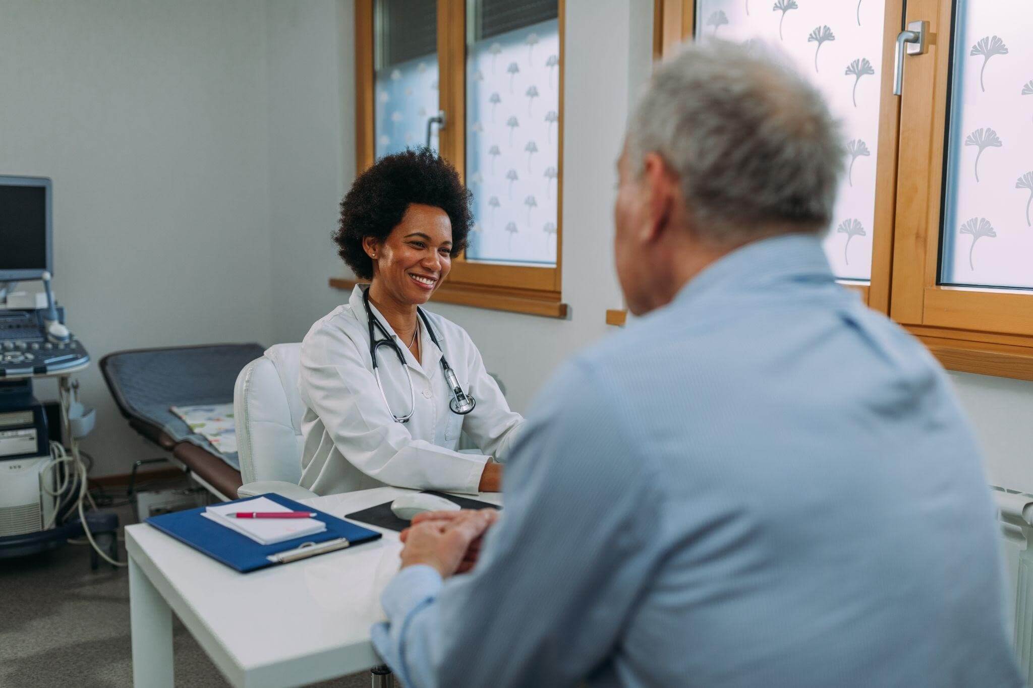 Uma médica sorridente conversa com um paciente em seu consultório, exemplificando a importância do acompanhamento médico especializado para o diagnóstico e tratamento de doenças autoimunes.
