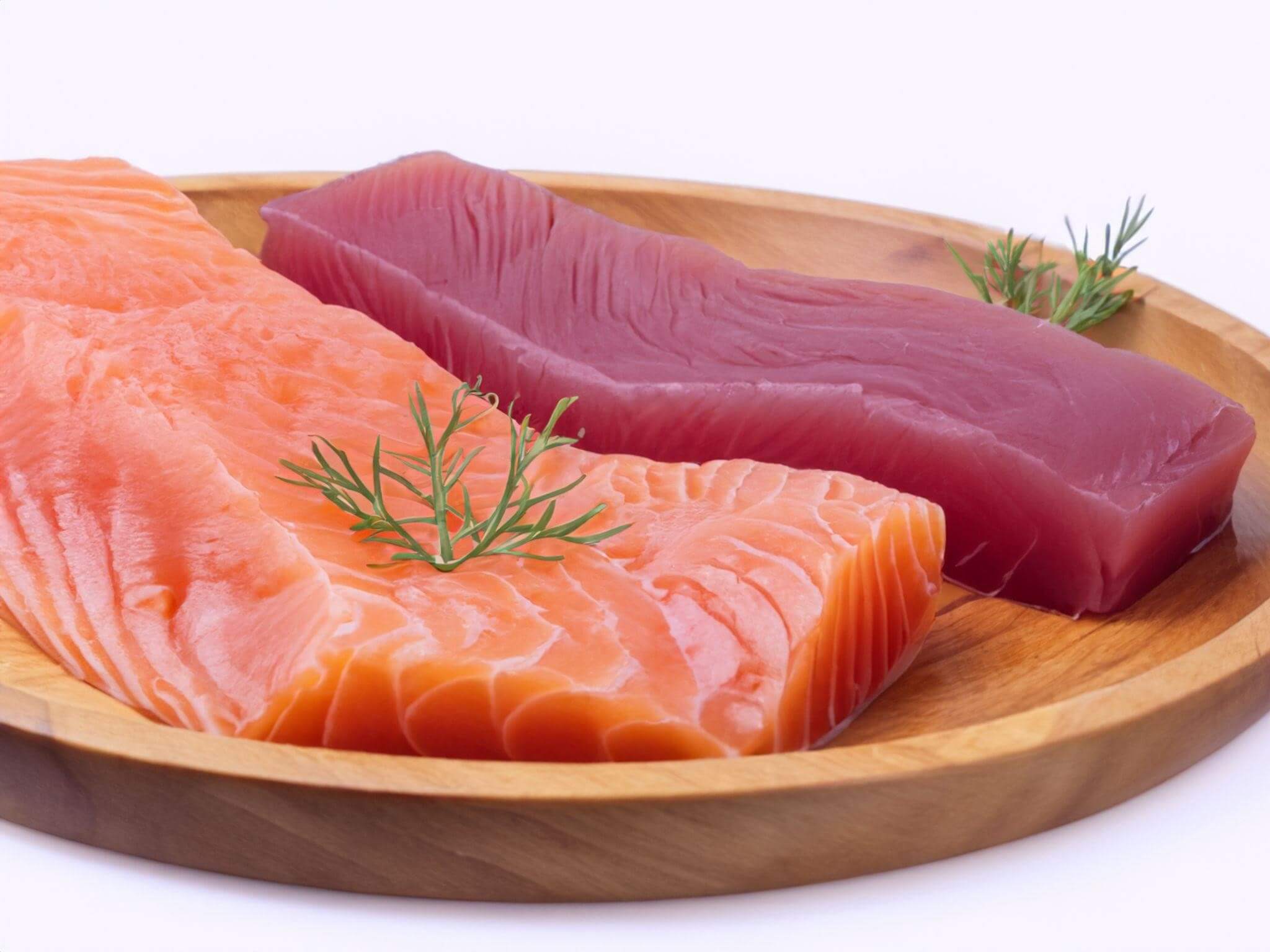 Close de postas frescas de salmão e atum em um prato de madeira. Peixes ricos em ômega-3 são aliados fundamentais na prevenção de doenças do coração e no controle do colesterol.