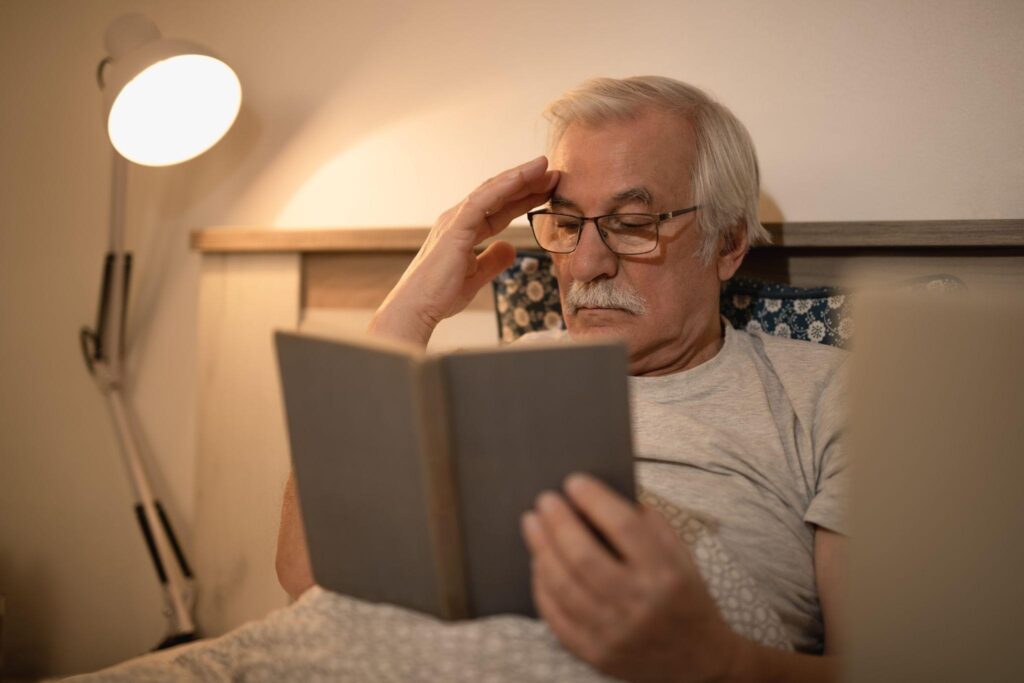 Idoso em seu quarto lendo um livro antes de dormir