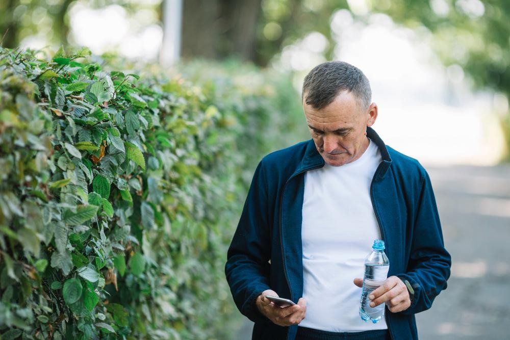 Homem com garrafa de água caminhando próximo a vegetação