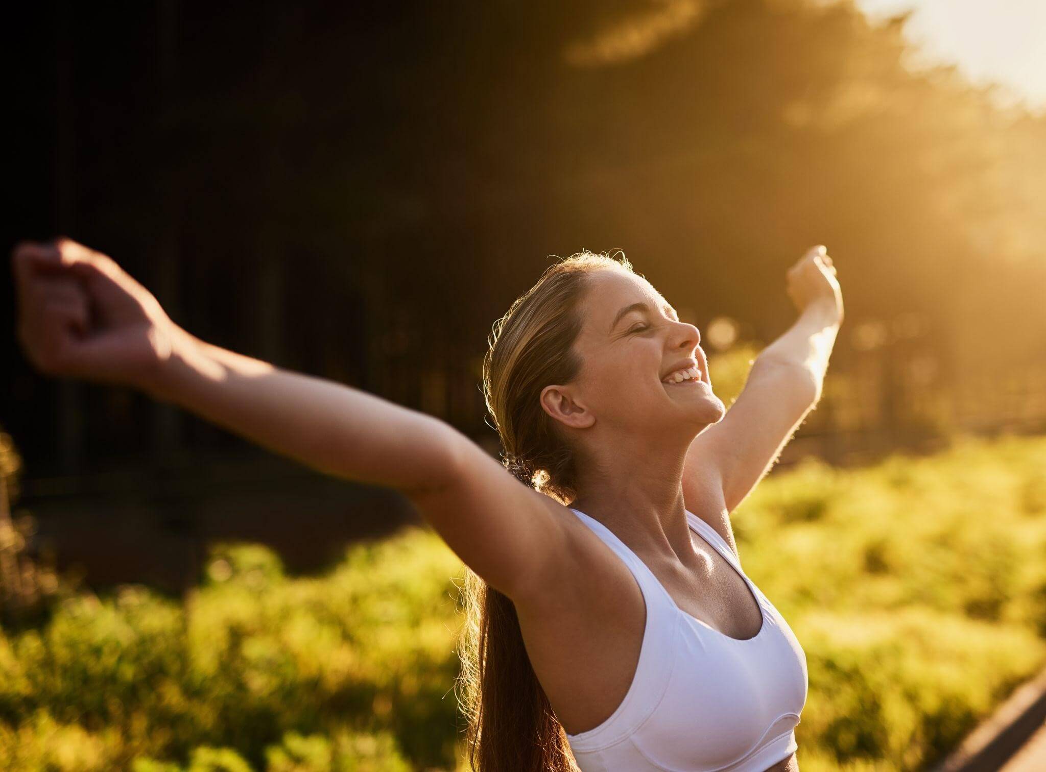 Mulher jovem sorrindo com os braços abertos em um campo ensolarado, representando a conquista de qualidade de vida e o bem-estar ao lidar com doenças autoimunes.