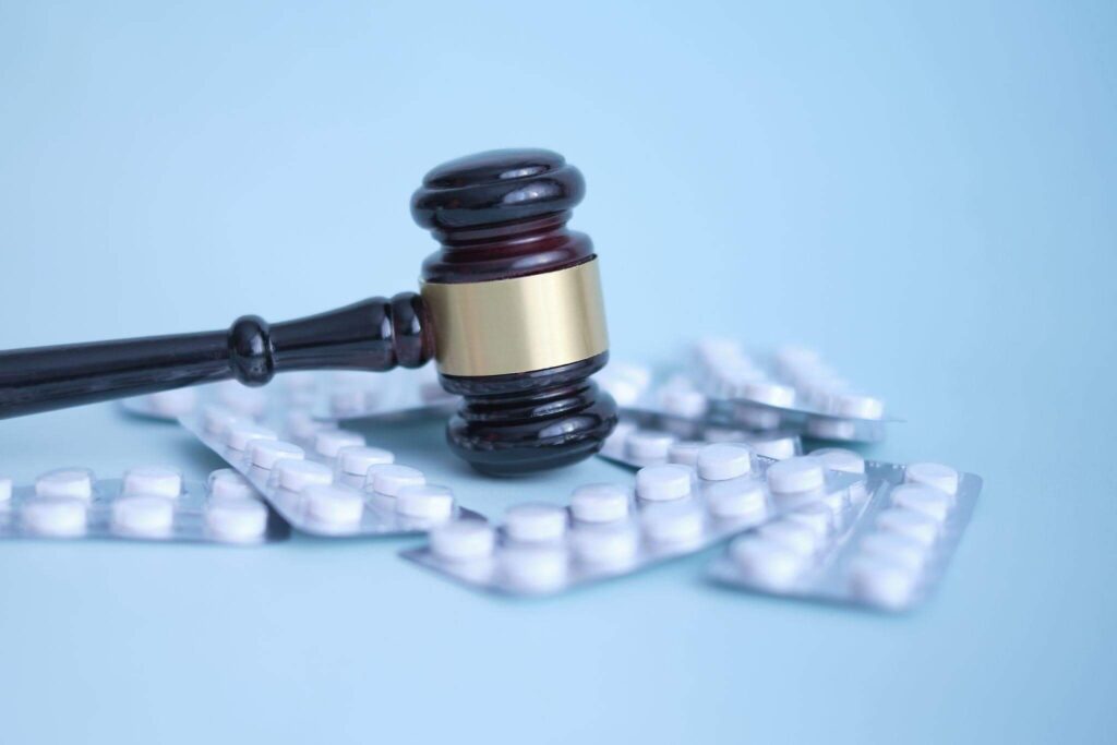 Close-up de um martelo de juiz de madeira repousando sobre várias cartelas de comprimidos brancos em um fundo azul, representando o processo judicial para obtenção de medicamentos de alto custo.